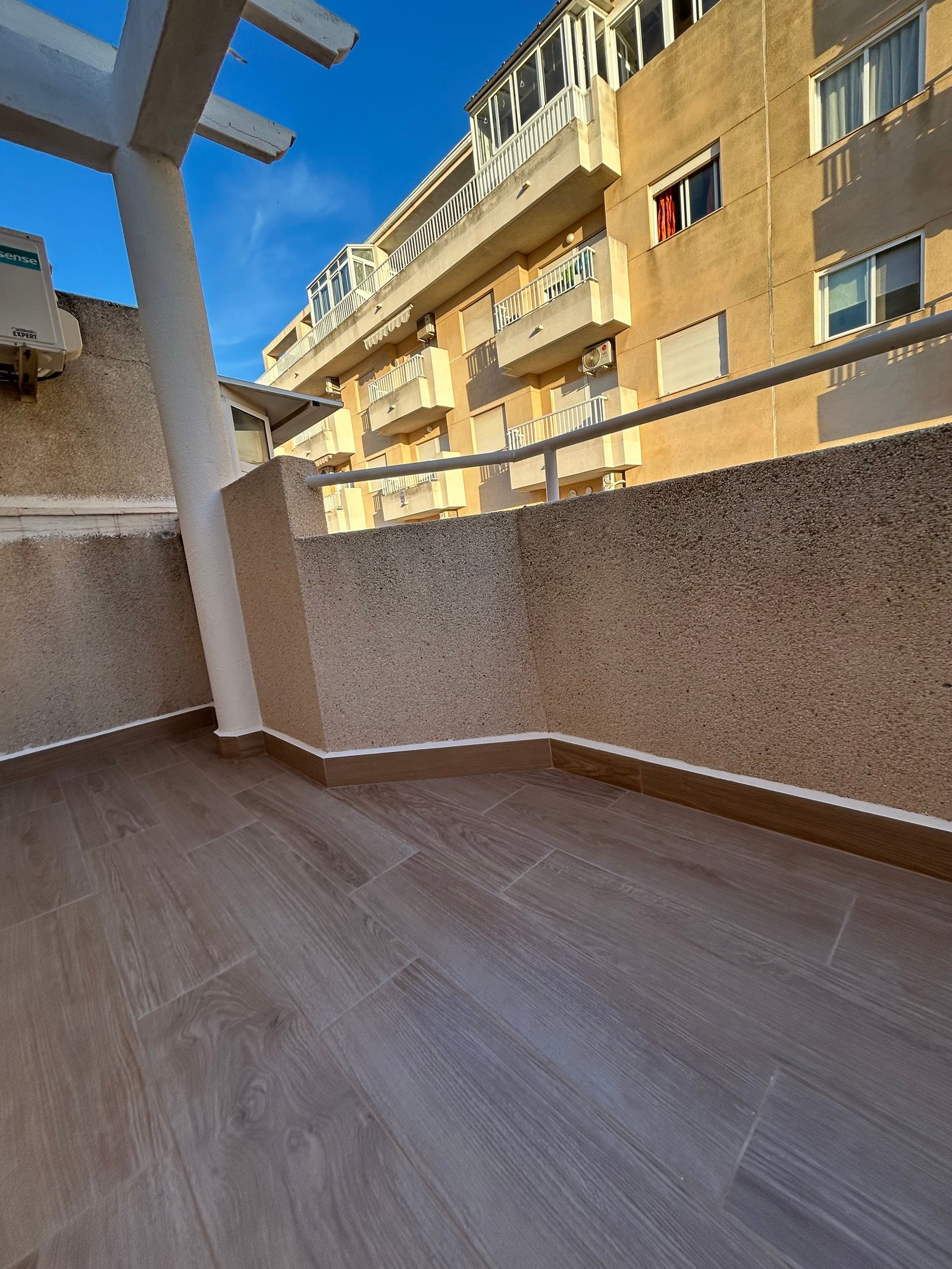 Balcón reformado con azulejo madera y techo pergola